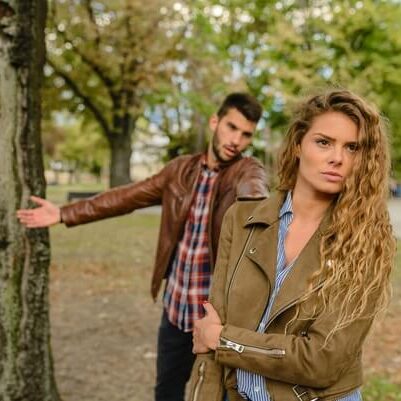 Angry woman walking away from man by tree