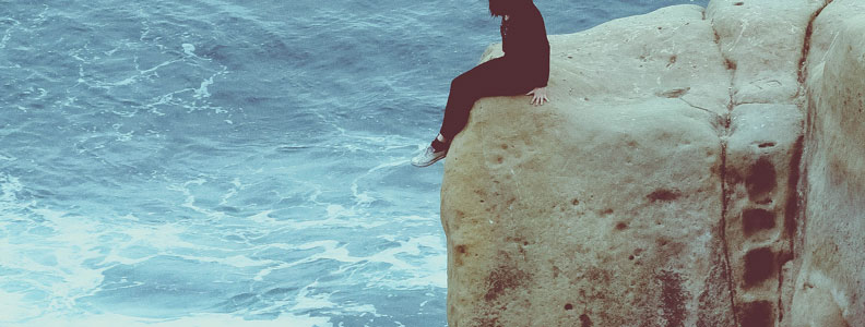woman sitting on cliff's edge by water