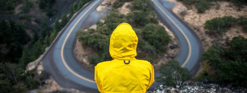 Man in raincoat on cliffside looking at road